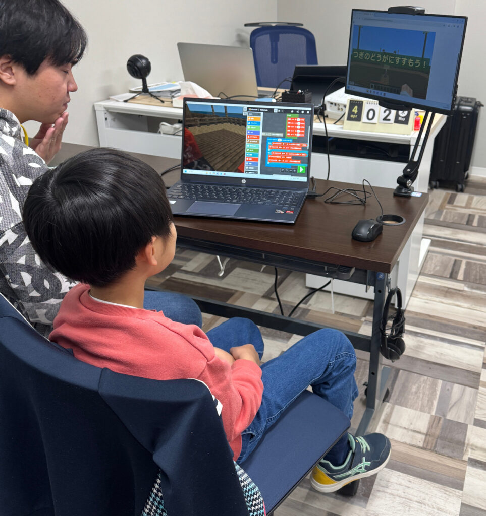 プログラミングのエラーに直面し、講師と一緒に原因を論理的に考えている小学生の様子